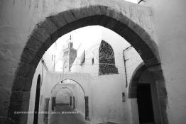 Image du Maroc Professionnelle de  Dans une rue des Habous, la succession des balèvres, moulure, arches, portiques et autres éléments décoratifs, projetent les visiteurs dans l’ardeur avec un élan de force et de fierté d’une époque révolue. Conçu par les architectes Auguste Cadet et Edmond Brion d’après l’ébauche d’un premier plan-masse dû à Albert Laprade, le quartier fait partie des endroits les plus pittoresques de Casablanca, il fut La construction n’avait commencé qu’après la première guerre mondiale. Situé près du Palais Royale, ce joyau architectural fait partie du patrimoine architectural de la ville, Lundi 12 Février 2007. Au centre le minaret de La mosquée Ben Youssef. (Photo / Abdeljalil Bounhar)
